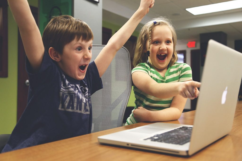 Boy with arms in air and girl pointing at laptop both looking excited